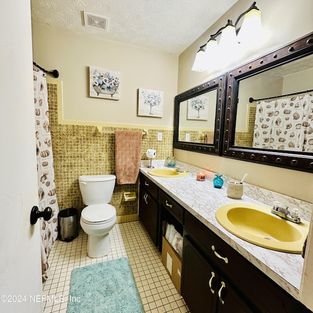 bathroom featuring vanity, tile patterned floors, toilet, a textured ceiling, and tile walls