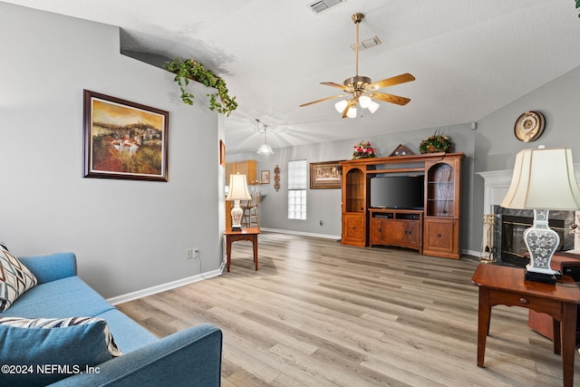 living room featuring ceiling fan, light wood-type flooring, a textured ceiling, and vaulted ceiling