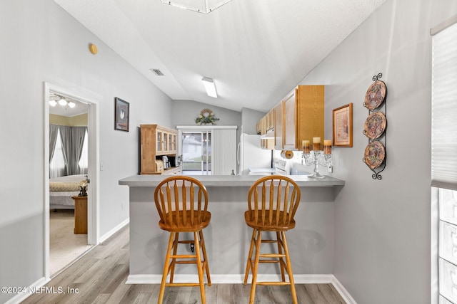 kitchen with kitchen peninsula, light hardwood / wood-style floors, white appliances, lofted ceiling, and a breakfast bar area