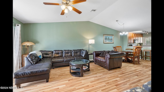 living room with ceiling fan with notable chandelier, light hardwood / wood-style floors, and vaulted ceiling