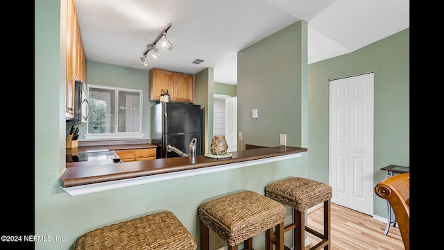 kitchen with black fridge, light wood-type flooring, and kitchen peninsula