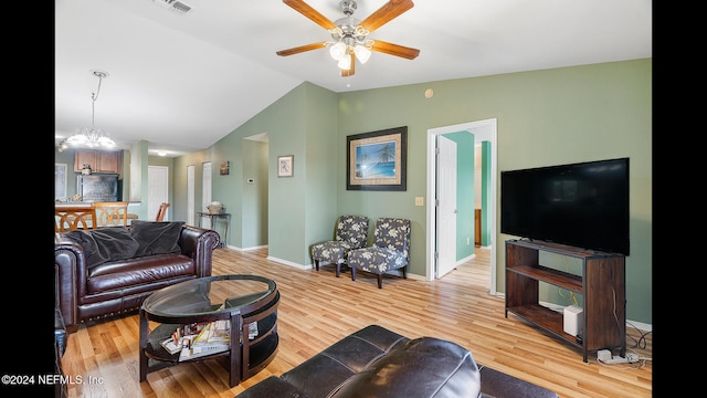 living room with ceiling fan with notable chandelier, light wood-type flooring, and lofted ceiling