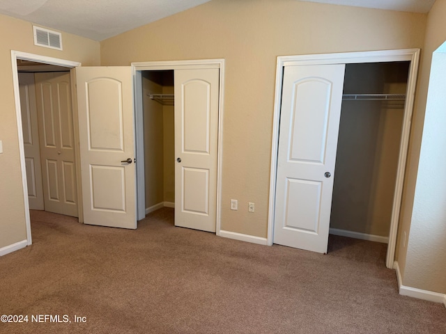 unfurnished bedroom featuring lofted ceiling, light carpet, and two closets