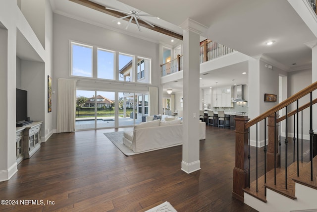 living room with a towering ceiling, dark hardwood / wood-style floors, ceiling fan, and crown molding