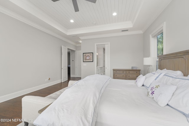 bedroom with ensuite bath, ceiling fan, dark wood-type flooring, a tray ceiling, and ornamental molding