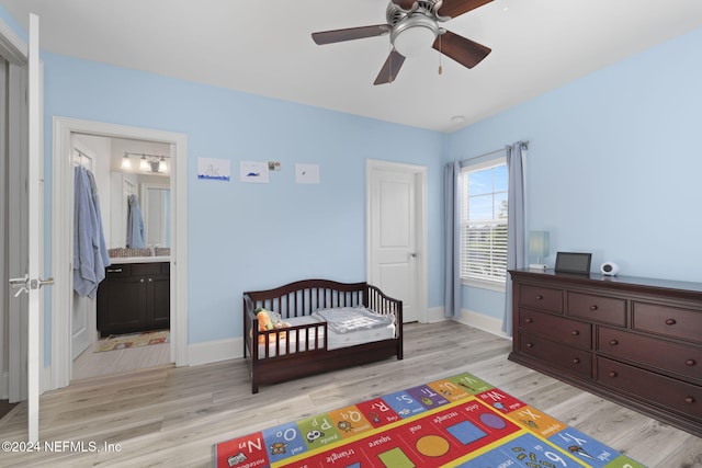 bedroom featuring a nursery area, ensuite bathroom, light hardwood / wood-style flooring, and ceiling fan