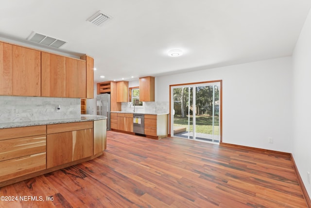 kitchen with backsplash, light stone countertops, stainless steel appliances, and hardwood / wood-style flooring