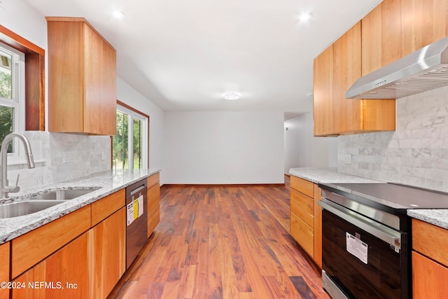 kitchen with light stone counters, light wood-type flooring, wall chimney range hood, and appliances with stainless steel finishes