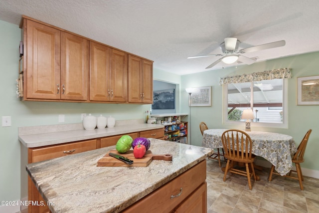 kitchen featuring light stone countertops, a textured ceiling, a kitchen island, and ceiling fan