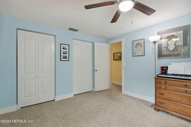 carpeted bedroom featuring ceiling fan, a textured ceiling, and two closets