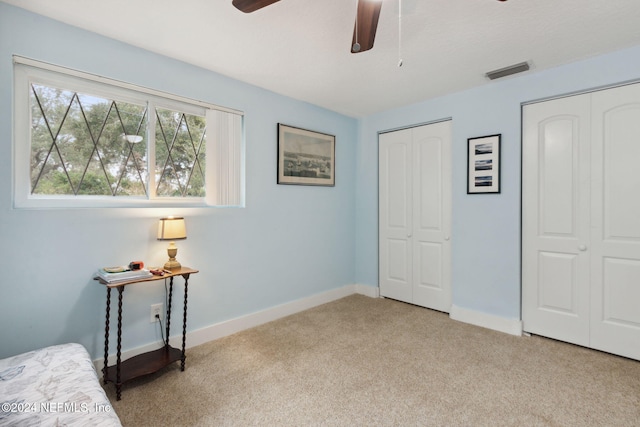 carpeted bedroom featuring ceiling fan and multiple closets