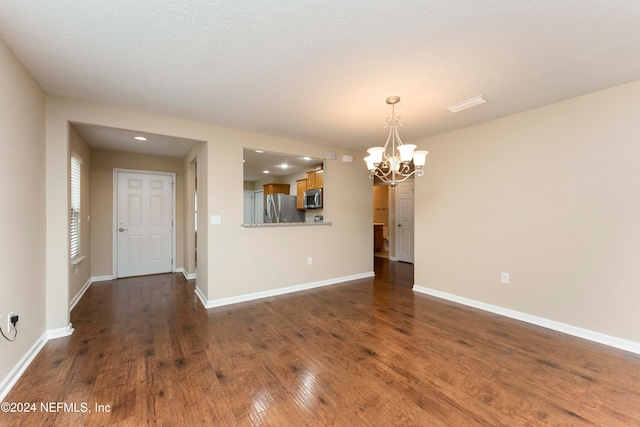 spare room with a chandelier, a textured ceiling, and dark hardwood / wood-style floors