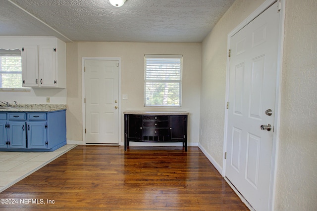 interior space with a textured ceiling, a textured wall, dark wood-type flooring, and baseboards