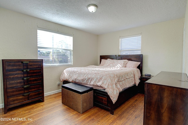 bedroom featuring baseboards, a textured wall, light wood-style flooring, and a textured ceiling