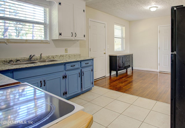 kitchen with light tile patterned floors, a sink, white cabinetry, a wealth of natural light, and freestanding refrigerator