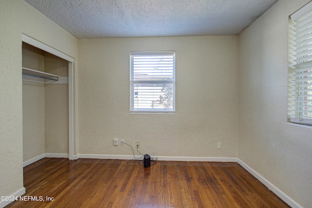 unfurnished bedroom featuring a textured ceiling, baseboards, dark wood-type flooring, and a textured wall