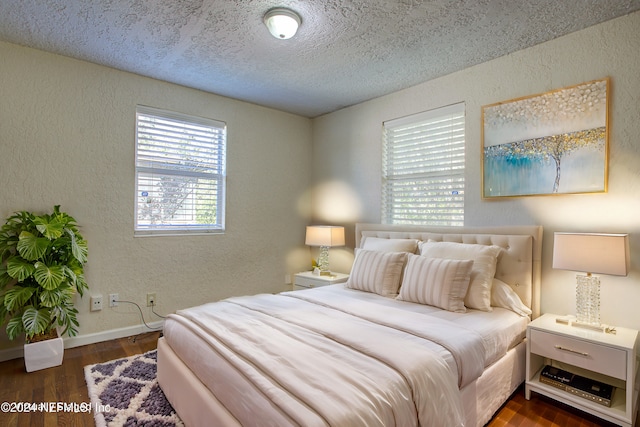 bedroom with a textured ceiling, a textured wall, dark wood-style flooring, and baseboards