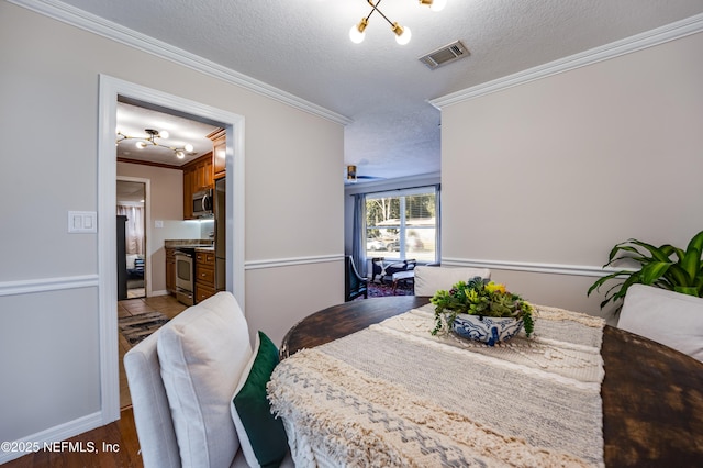 dining space with wood-type flooring, a textured ceiling, ornamental molding, and a notable chandelier