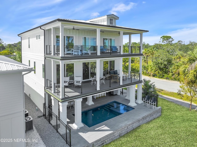 rear view of property with board and batten siding, an outdoor pool, a balcony, ceiling fan, and a patio area