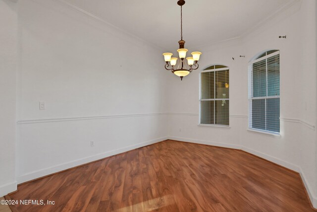 unfurnished room with hardwood / wood-style flooring, an inviting chandelier, and ornamental molding