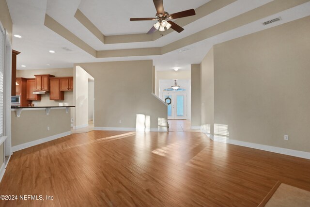 unfurnished living room featuring a tray ceiling, ceiling fan, and light hardwood / wood-style floors