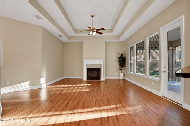 unfurnished living room with hardwood / wood-style flooring, ceiling fan, and a tray ceiling