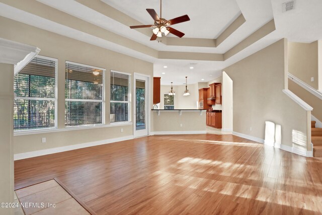 unfurnished living room featuring light hardwood / wood-style floors, ceiling fan, and a tray ceiling