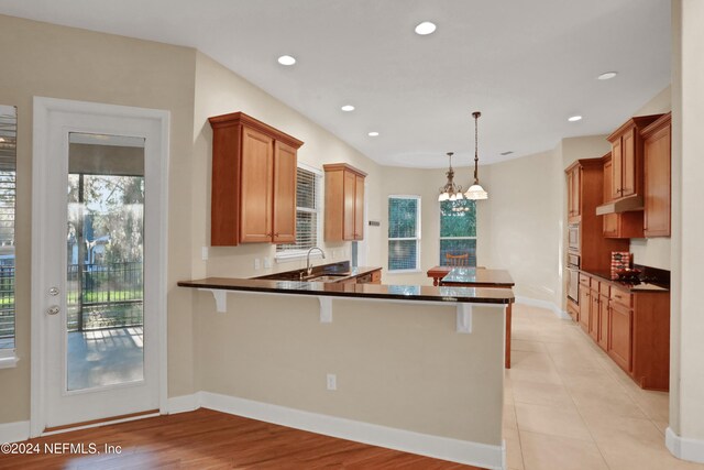 kitchen with sink, a kitchen breakfast bar, kitchen peninsula, decorative light fixtures, and light wood-type flooring