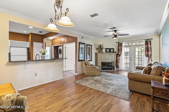 living room featuring a tiled fireplace, ceiling fan, crown molding, and light hardwood / wood-style floors