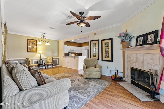 living room featuring light hardwood / wood-style floors, ceiling fan, crown molding, and a tiled fireplace