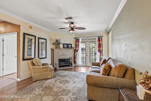 living room with ceiling fan, wood-type flooring, crown molding, and a tiled fireplace