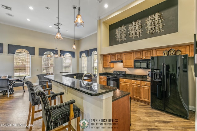 kitchen with a kitchen breakfast bar, light hardwood / wood-style flooring, crown molding, pendant lighting, and black appliances