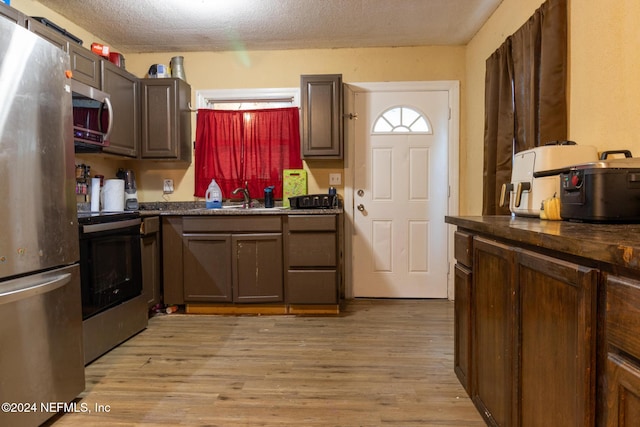 kitchen featuring light wood-type flooring, dark brown cabinets, a textured ceiling, stainless steel appliances, and sink