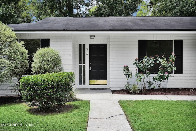 view of exterior entry featuring a lawn and a porch