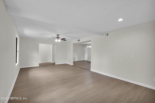 empty room featuring a textured ceiling, ceiling fan with notable chandelier, and dark hardwood / wood-style floors