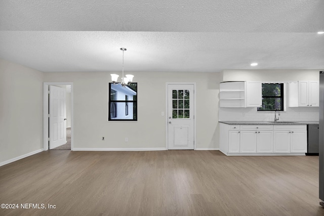 unfurnished dining area with a textured ceiling, sink, a notable chandelier, and light wood-type flooring