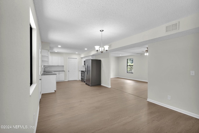 kitchen featuring appliances with stainless steel finishes, light wood-type flooring, ceiling fan with notable chandelier, white cabinets, and hanging light fixtures