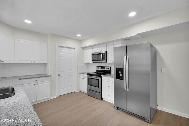 kitchen featuring light stone countertops, appliances with stainless steel finishes, backsplash, white cabinets, and light hardwood / wood-style floors