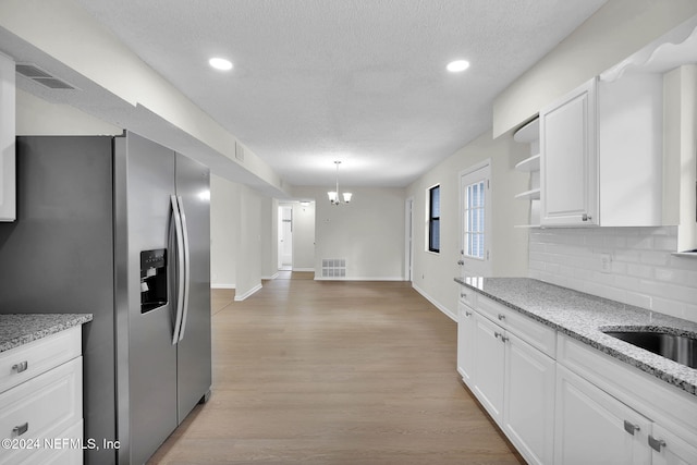 kitchen with white cabinetry, stainless steel refrigerator with ice dispenser, pendant lighting, decorative backsplash, and light wood-type flooring