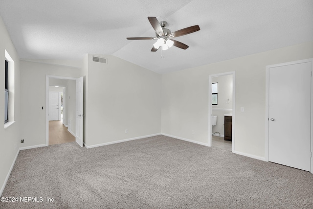 unfurnished bedroom featuring ensuite bath, ceiling fan, light colored carpet, a textured ceiling, and vaulted ceiling