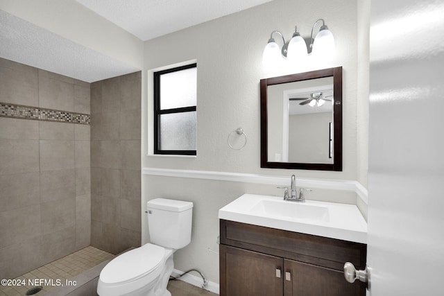 bathroom with a tile shower, a textured ceiling, vanity, ceiling fan, and toilet