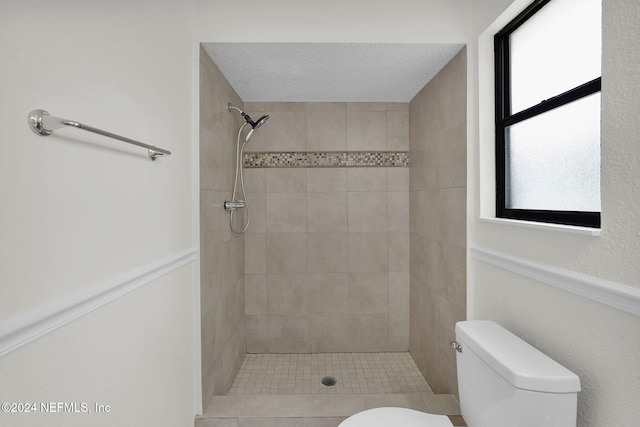 bathroom featuring a textured ceiling, a healthy amount of sunlight, toilet, and tiled shower