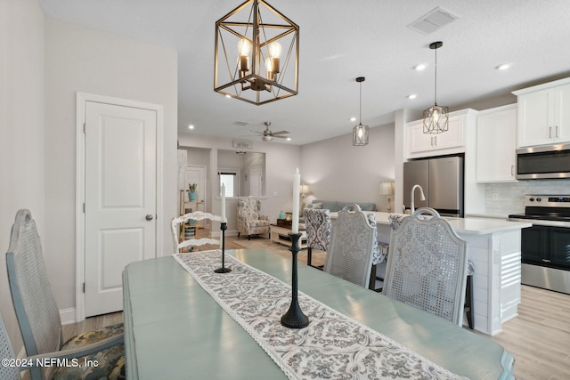 dining space with ceiling fan with notable chandelier and light hardwood / wood-style floors