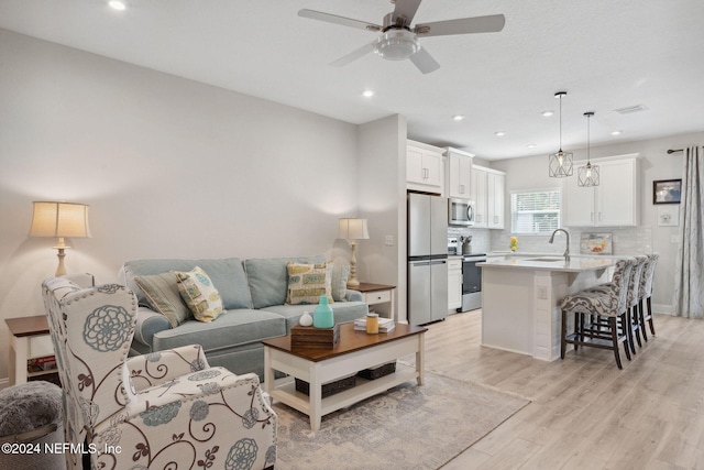 living room featuring ceiling fan, sink, and light wood-type flooring