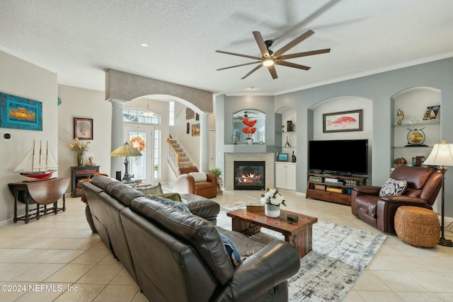 tiled living room featuring built in shelves, a textured ceiling, ornamental molding, and a tiled fireplace