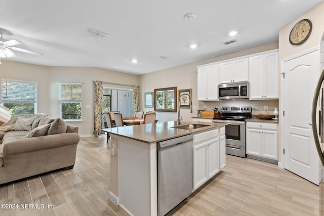 kitchen with light wood-type flooring, stainless steel appliances, white cabinetry, and an island with sink