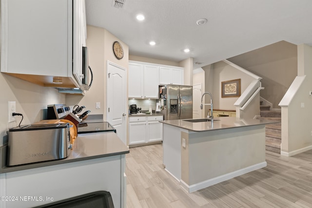 kitchen with appliances with stainless steel finishes, a kitchen island with sink, sink, light hardwood / wood-style flooring, and white cabinets