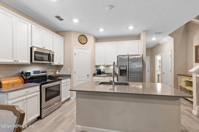 kitchen with white cabinetry, an island with sink, appliances with stainless steel finishes, and light hardwood / wood-style flooring