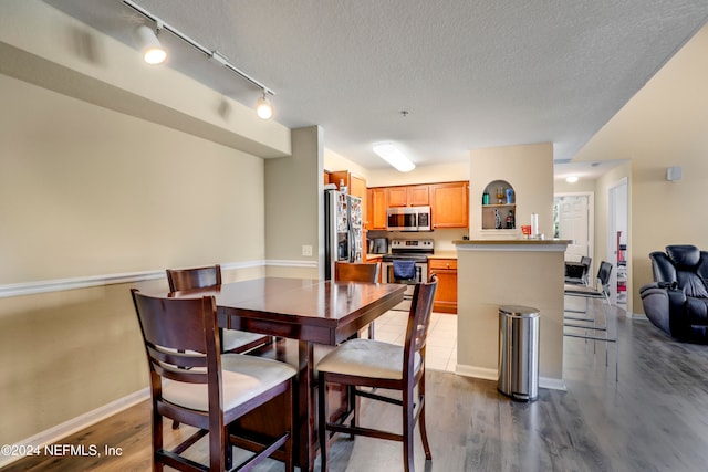 dining room with dark hardwood / wood-style flooring, track lighting, and a textured ceiling