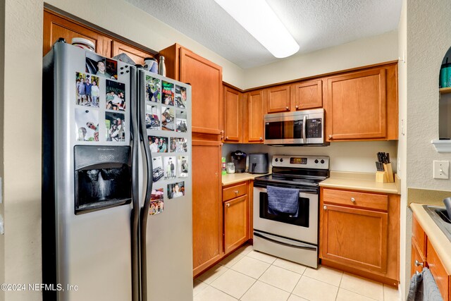 kitchen with light tile patterned floors, a textured ceiling, and appliances with stainless steel finishes